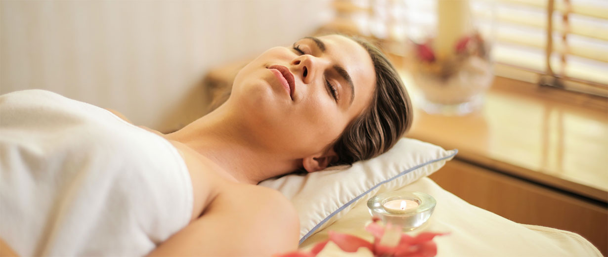 A woman resting on a bed with her eyes closed, embodying relaxation and tranquility at Melody Salon.
